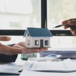 Majiteľ domu podpisuje poistnú zmluvu s poradcom pri stole s modelom domu